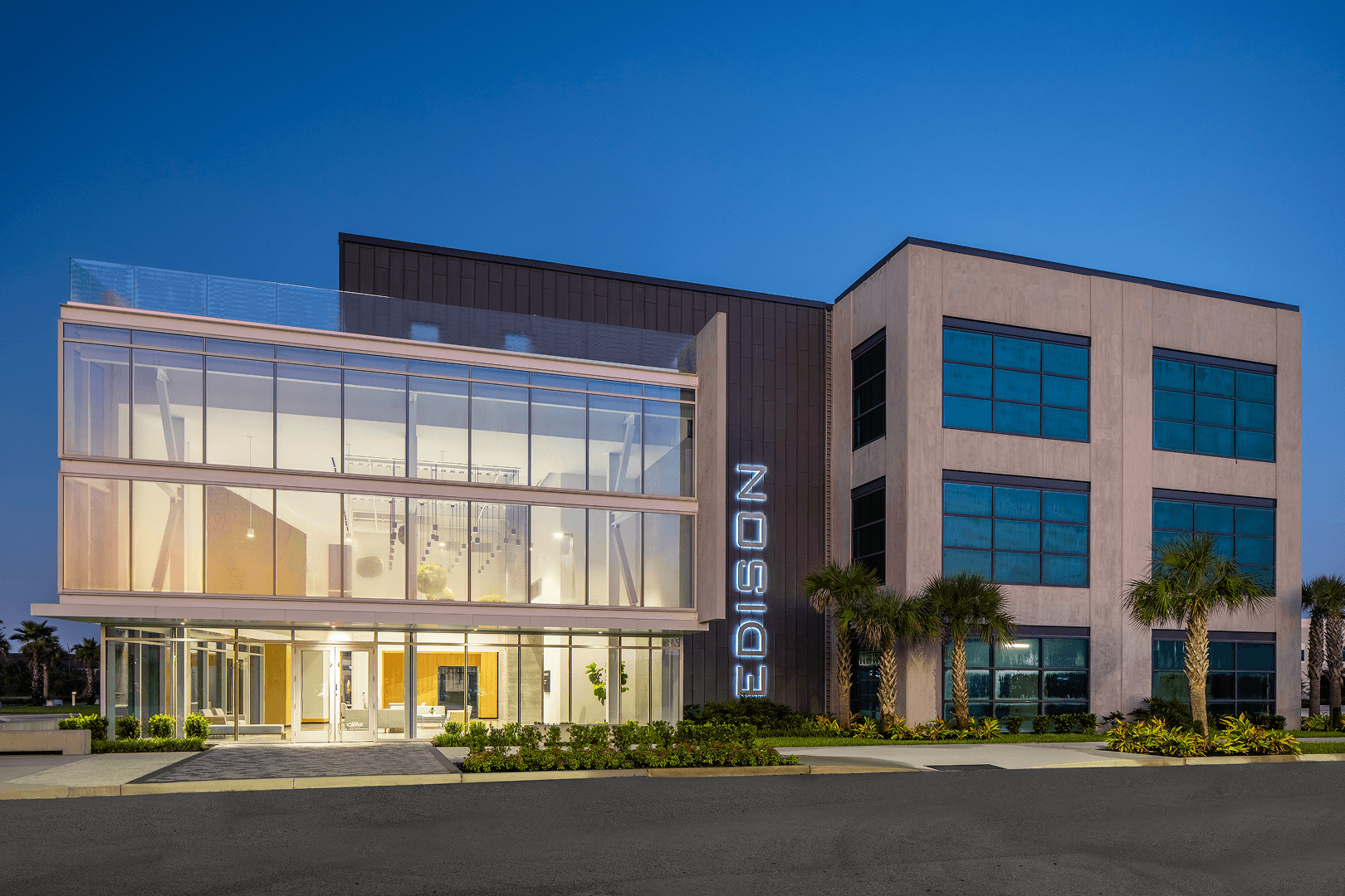 Modern Edison Office Building Exterior at Dusk Contemporary three-story Edison office building with glass facade, illuminated interiors, and palm tree landscaping at twilight.