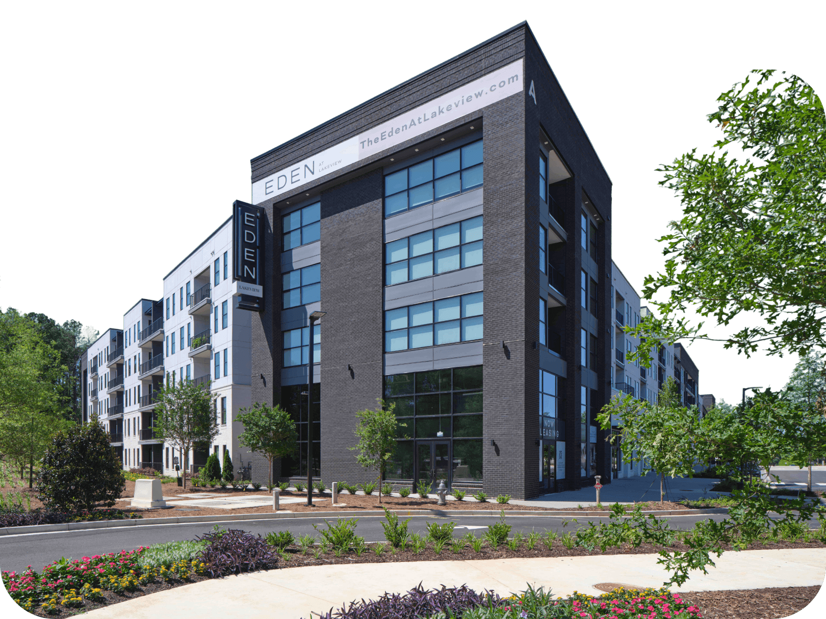 Eden Lakeview Modern Apartment Building Front View Modern multi-story Eden apartment building with dark brick facade, large windows, and landscaped grounds with trees and flowers.