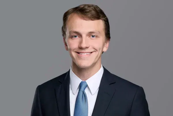 Max Armstrong Professional Headshot Portrait Professional headshot of Max Armstrong, a young man in a navy suit with blue tie, smiling at camera against gray background