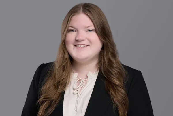 Maggie Barronton Professional Headshot Portrait Professional headshot of Maggie Barronton wearing a black blazer over a cream blouse, smiling at camera against gray background