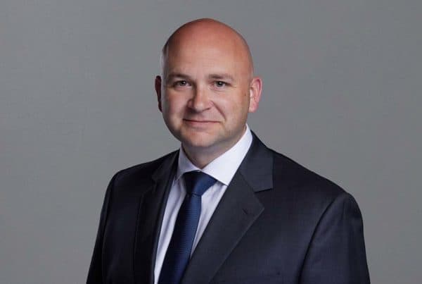 Professional Portrait of Callaway W. Professional headshot of a bald businessman in a dark suit and blue tie against a gray background