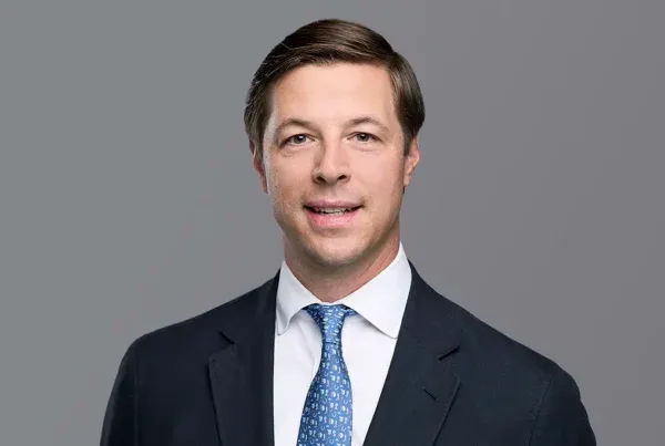 Will Corbitt Professional Business Portrait Professional headshot of Will Corbitt wearing a navy suit, white shirt, and blue patterned tie against a gray background