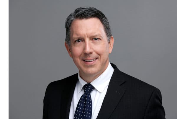 John Crane Professional Business Portrait Headshot Professional headshot of John Crane in dark suit and patterned tie, smiling against gray background