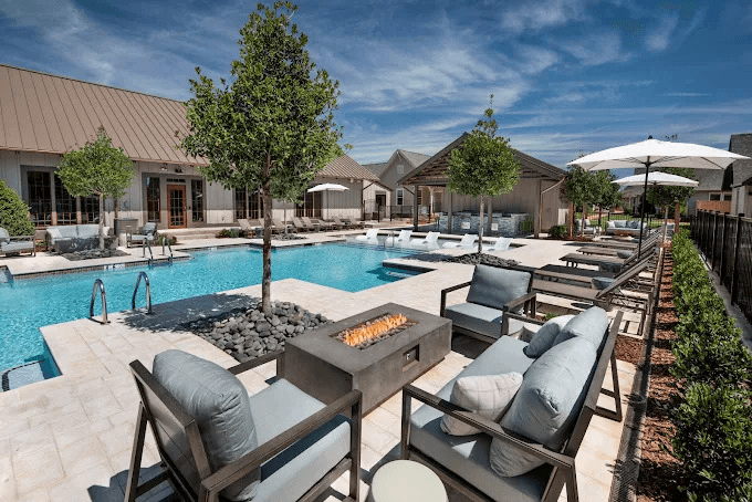 Luxury Pool Area with Modern Outdoor Amenities Modern resort-style pool with lounge chairs, fire pit seating area, and residential buildings under blue sky