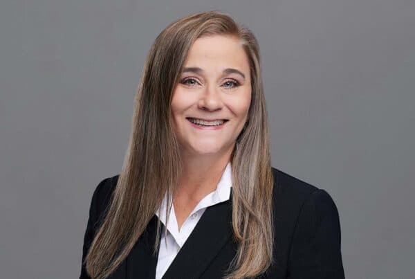 Holland R. Professional Business Portrait Professional headshot of Holland R. smiling, wearing a black blazer and white collared shirt against a gray background.