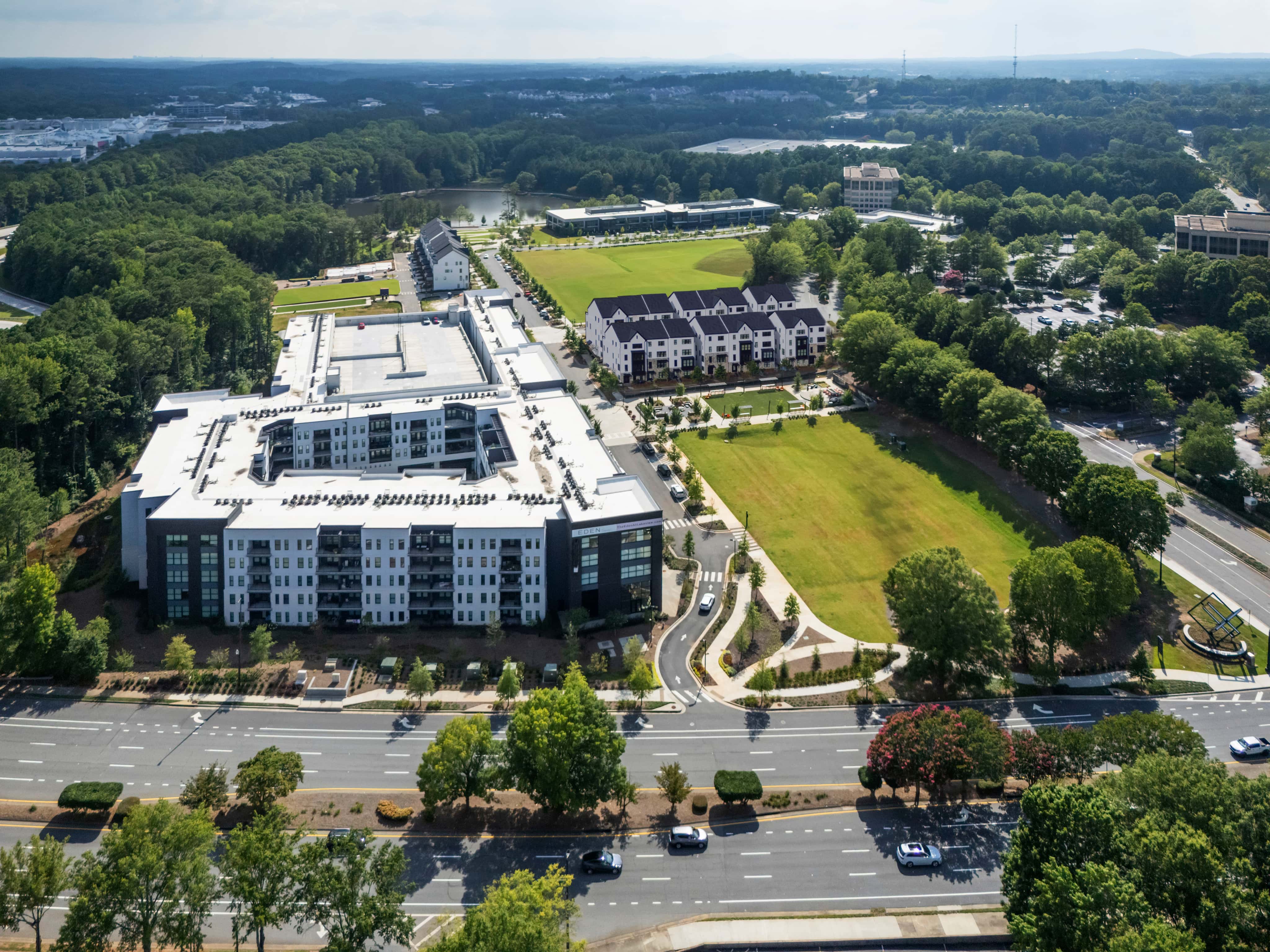 Aerial View of Master-Planned Community Development Aerial photograph showing modern apartment buildings, green spaces, curved roads, and landscaping in a master-planned residential community surrounded by trees.