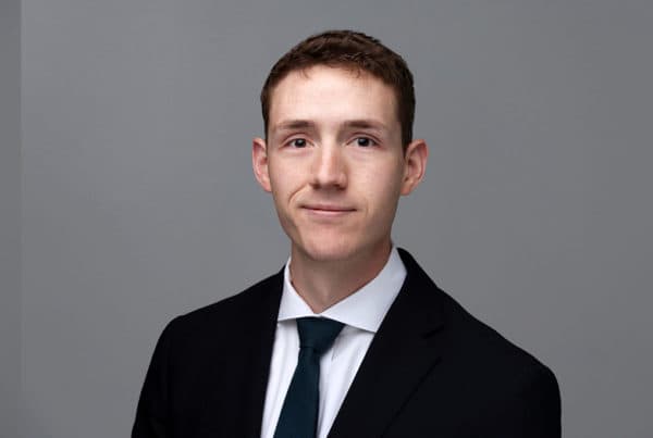 Kennan O'Brien Professional Business Portrait Professional headshot of Kennan O'Brien wearing a black suit, white shirt, and dark tie against a gray background.