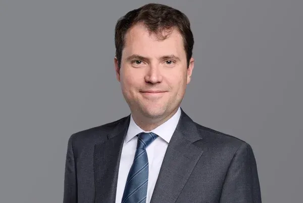 Prince Matt Professional Business Portrait Photo Professional headshot of Prince Matt wearing a dark suit and blue striped tie against a gray background