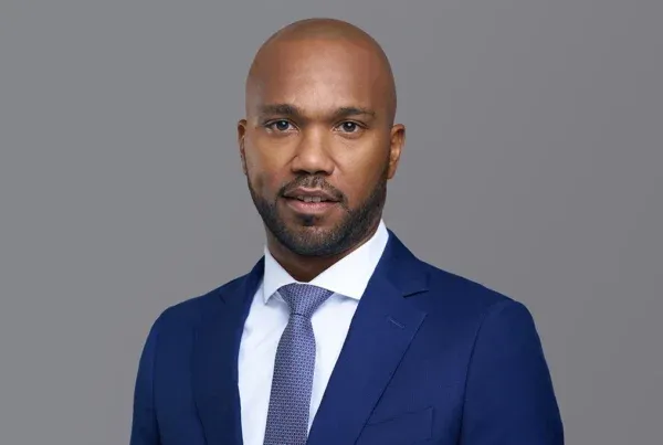 Rashid A. Professional Business Portrait Professional headshot of Rashid A., a bald man with beard wearing a navy blue suit and patterned tie against gray background