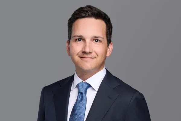 Dominic Reinecker Professional Business Portrait Professional headshot of Dominic Reinecker in a dark navy suit with blue tie against a gray background