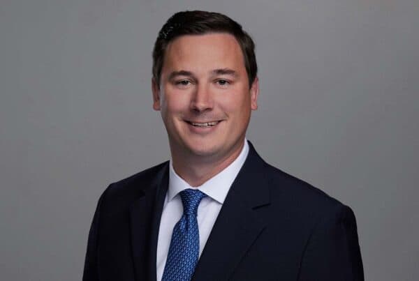 Professional Business Portrait of Rittle S. Professional headshot of a smiling man in a dark suit with blue tie against a gray background
