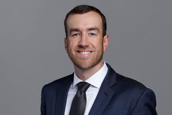 Professional Headshot of Snyder B Professional business portrait of a smiling man in a navy suit and tie against a gray background