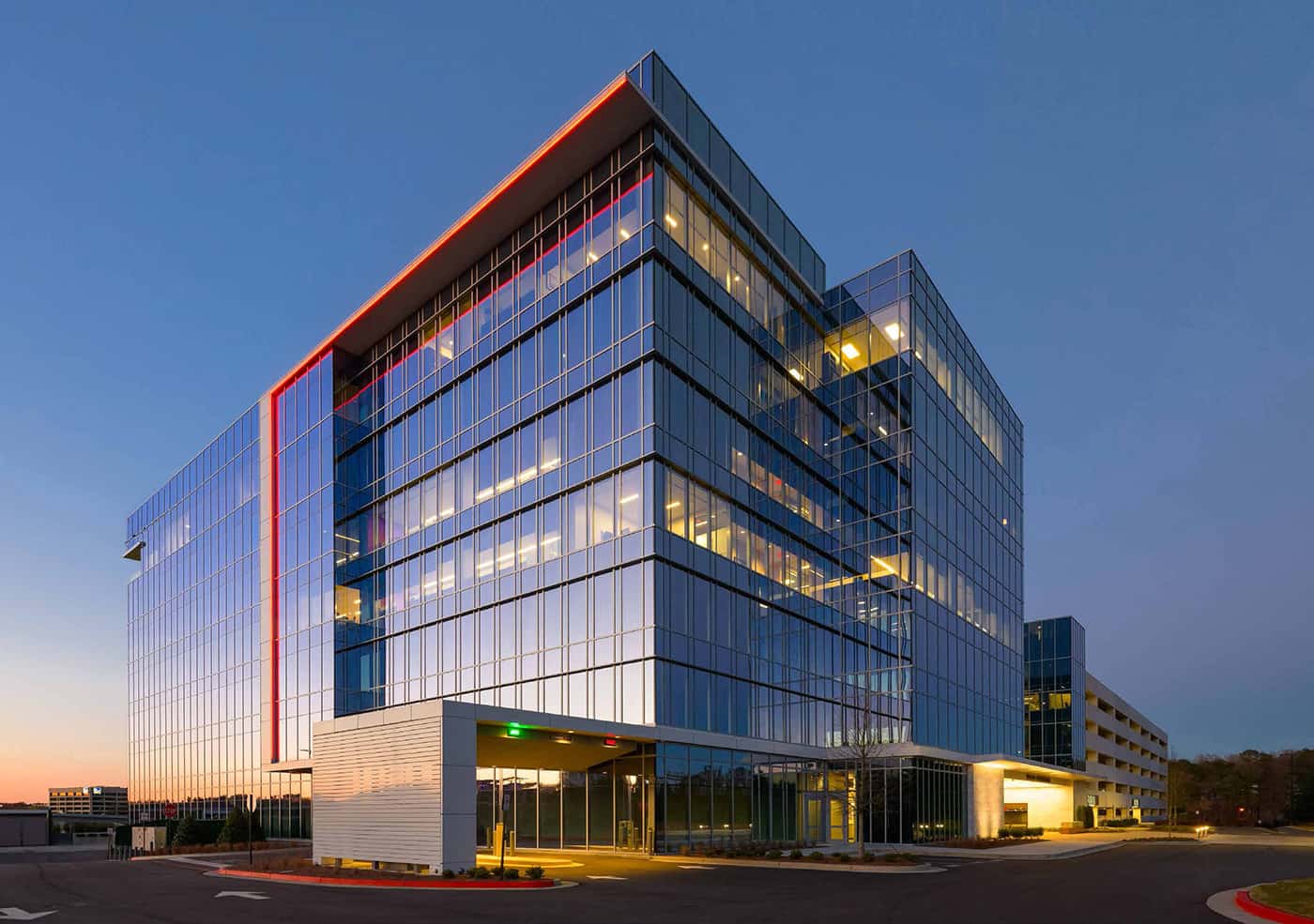 Modern Glass Office Building at Dusk Contemporary multi-story glass office building with illuminated interior and orange accent lighting at twilight, showcasing strategic architectural vision.
